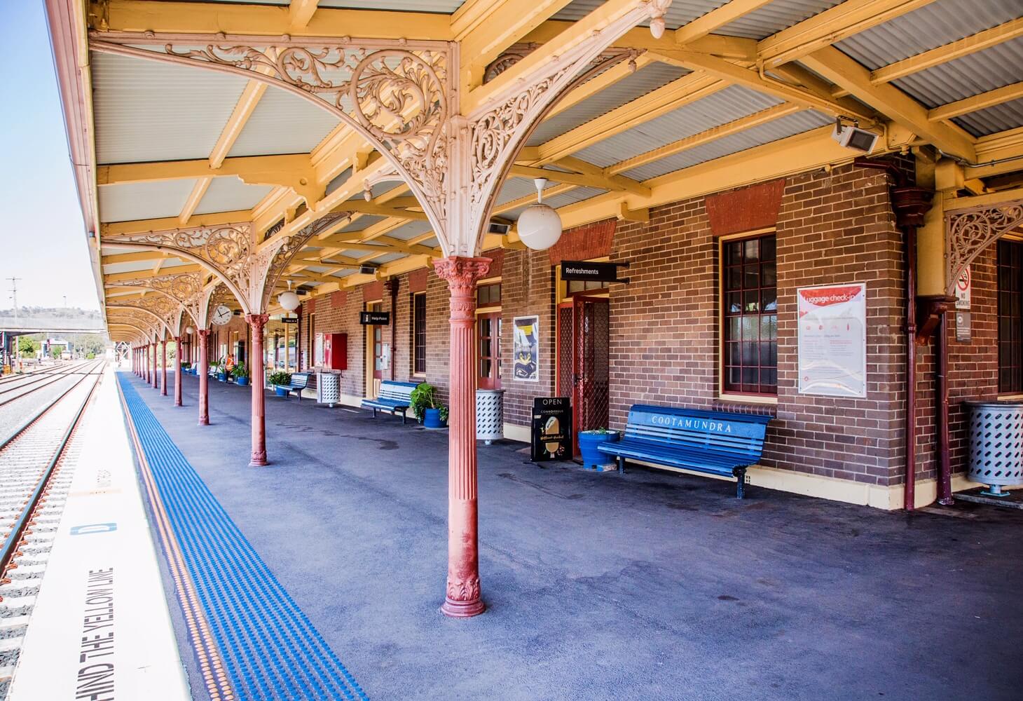 A photo of the train platform at the Cootamundra railway station. The train tracks are in the far left of the picture with bench seats and the platform roof in the centre.