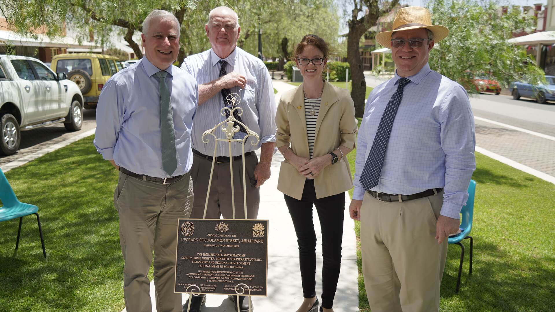 Michael McCormack, Nigel Judd, Steph Cooke and Rick Firman stand around a plaque which sits on an easel. Behind them is new grass and trees.