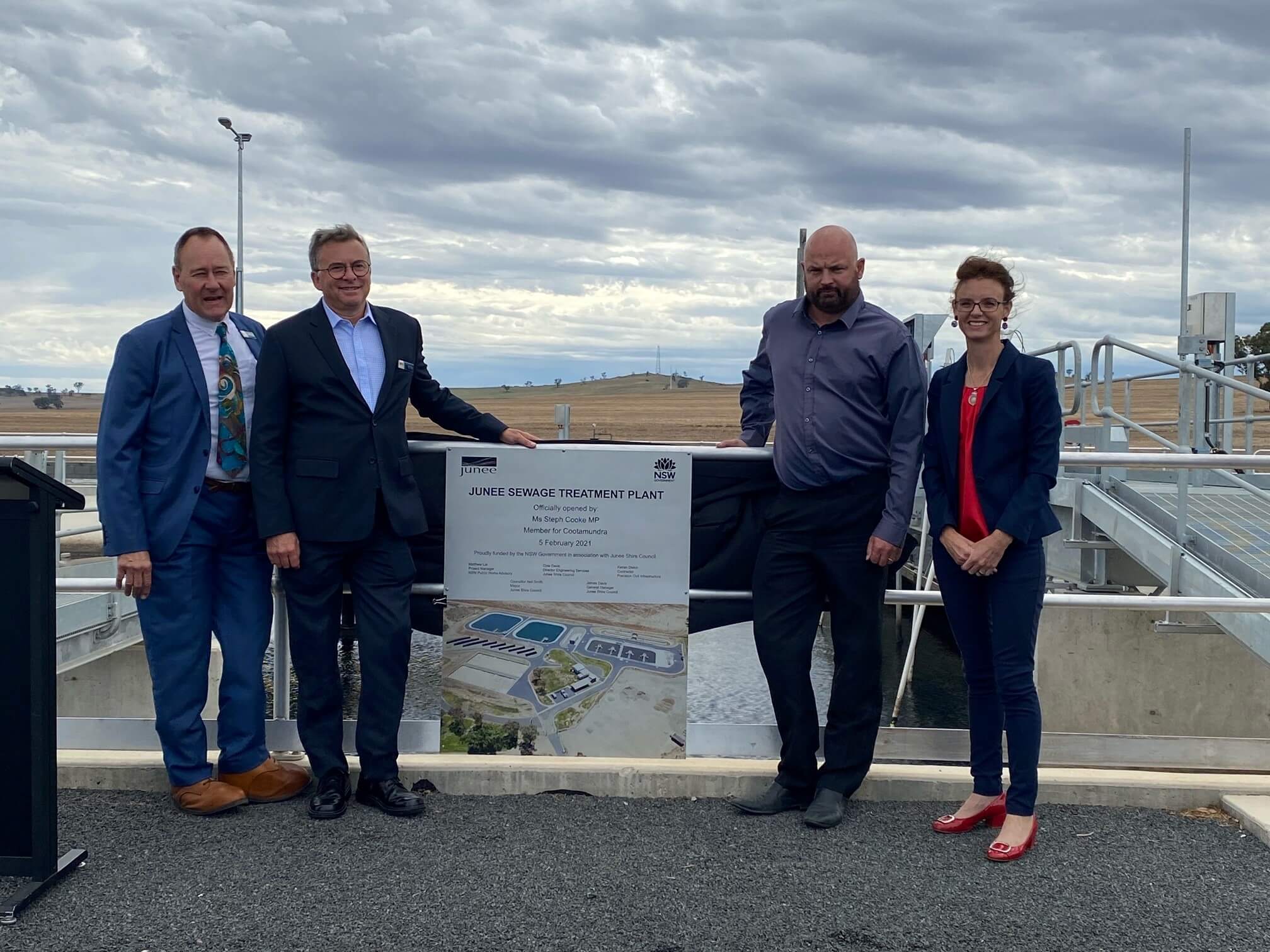 Cr Neil Smith, James Davis, Cole Davis and Steph Cooke MP stand next to a sign that reads 'Junee Sewerage Treatment Plant' and lean against a railing. Behind them is a pool of sewerage water.