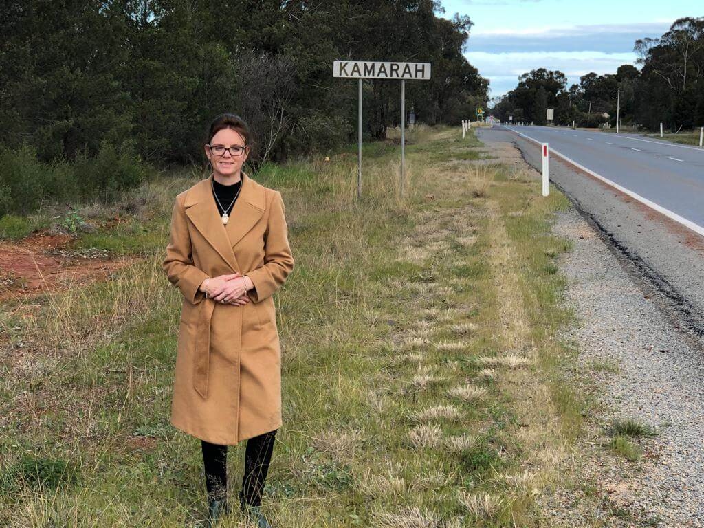 Steph Cooke stands beside a road. A sign says Kamarah behind her.