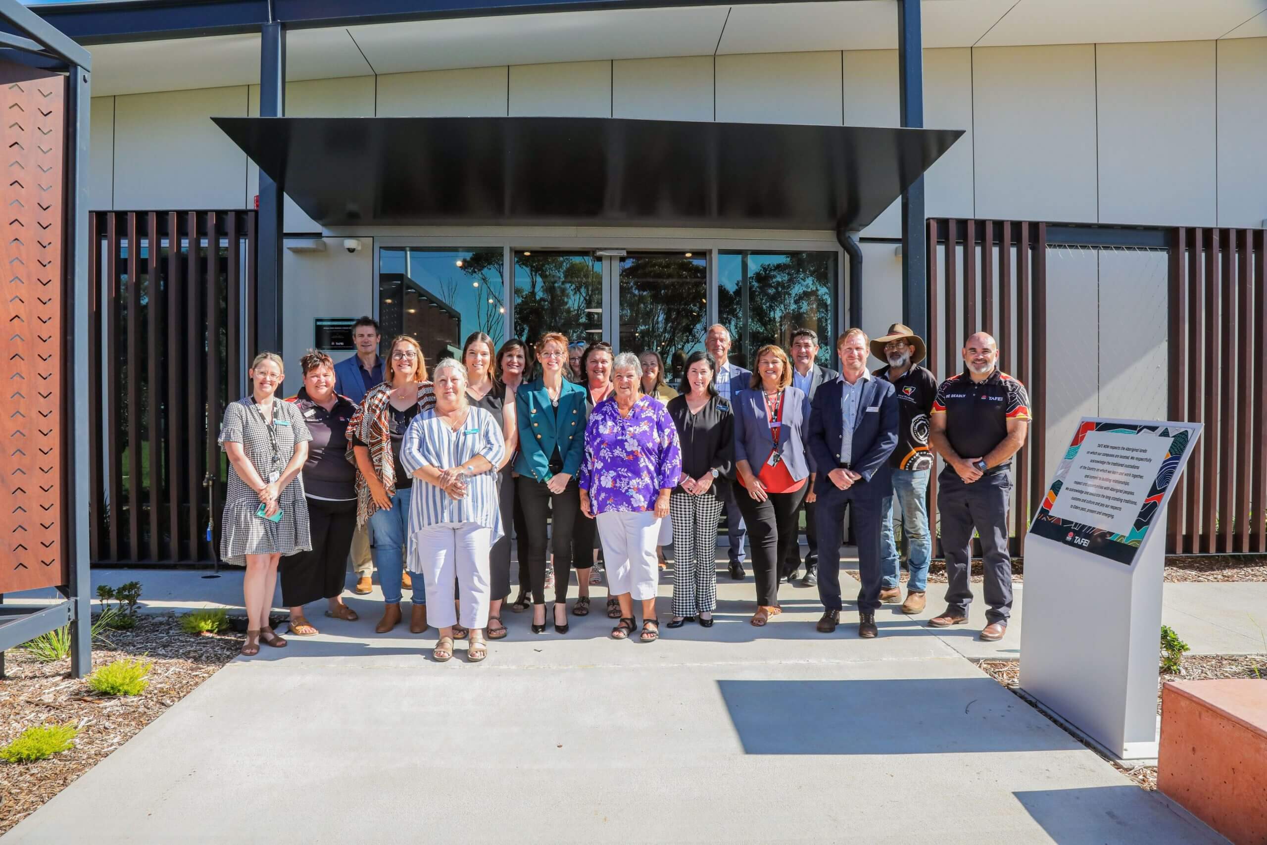 Steph Cooke and Minister Lee stand in a group of TAFE staff in front of a new building.